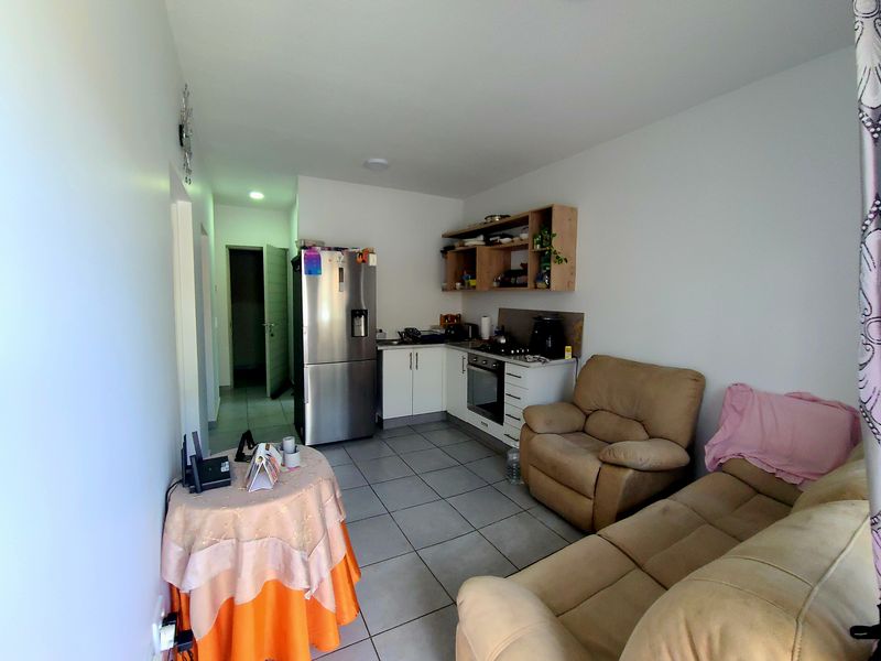 Open-plan living area featuring a compact kitchen with built-in cabinetry, oven, and hob, finished with tiled flooring throughout.