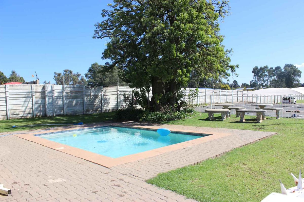 Outdoor pool area featuring a swimming pool, paved surround, lawn, and perimeter wall with electric fencing.