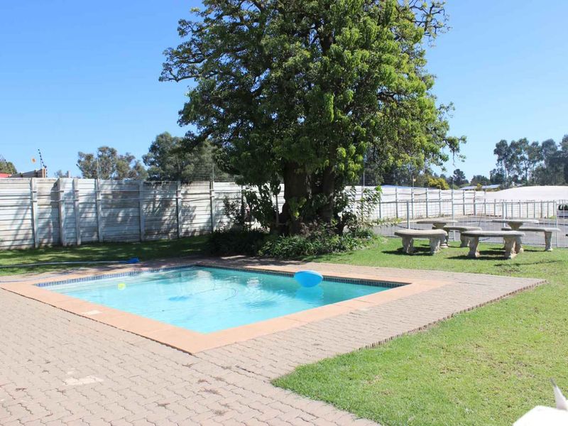 Outdoor pool area featuring a swimming pool, paved surround, lawn, and perimeter wall with electric fencing.