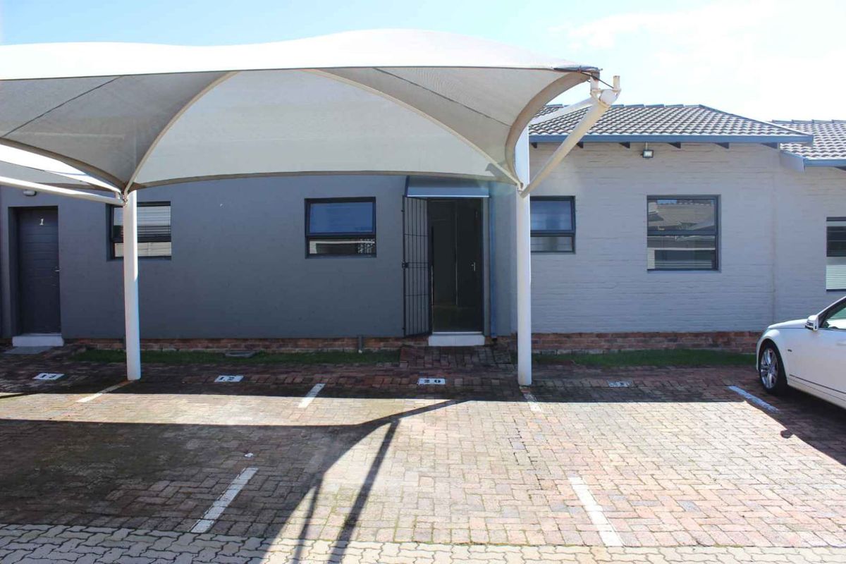 Front exterior view of the townhouse featuring a paved driveway, covered carport parking, and secure entrance access.