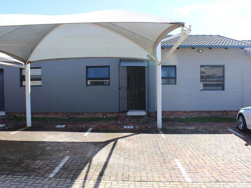 Front exterior view of the townhouse featuring a paved driveway, covered carport parking, and secure entrance access.