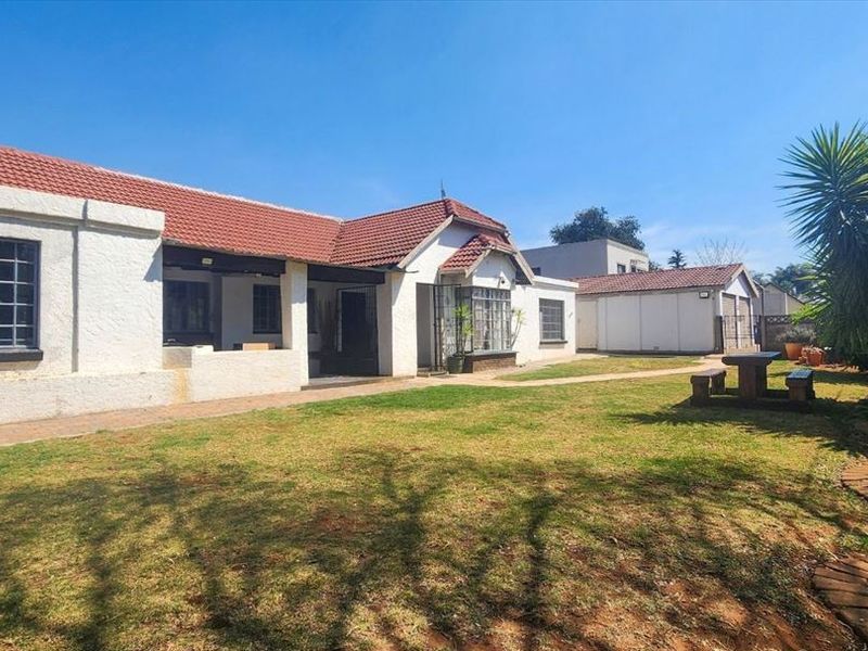 Rear view of the house featuring a tiled roof, paved walkway, and a spacious lawn area with an adjacent garage structure.