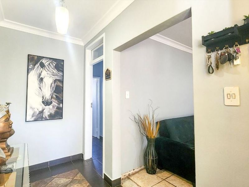 A bright entrance hallway featuring tiled flooring, cove cornicing, and a transition into an adjacent living space.