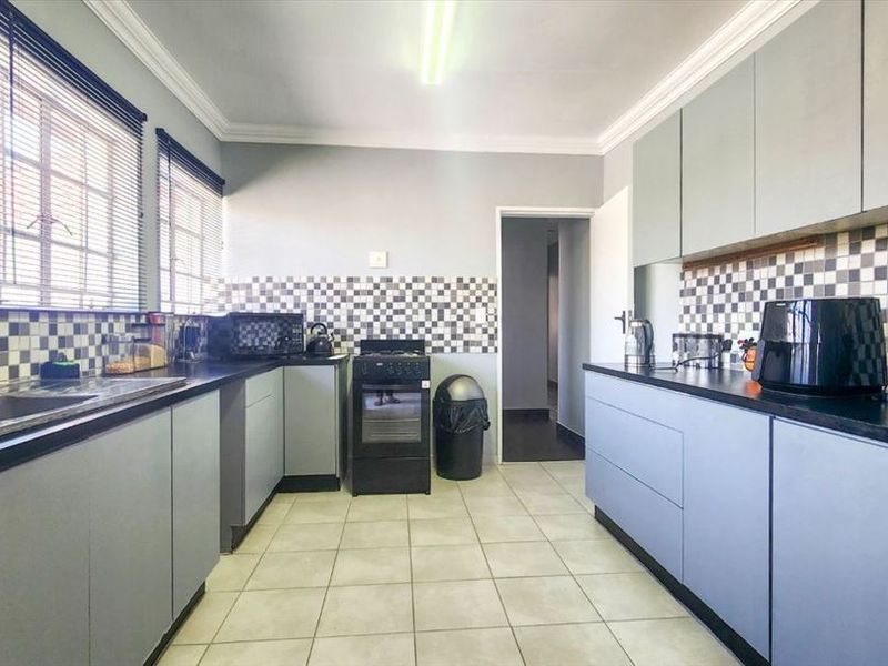 Functional kitchen featuring grey cabinetry, dark laminate countertops, a tiled backsplash, and ceramic floor tiles, providing a practical workspace with ample storage.