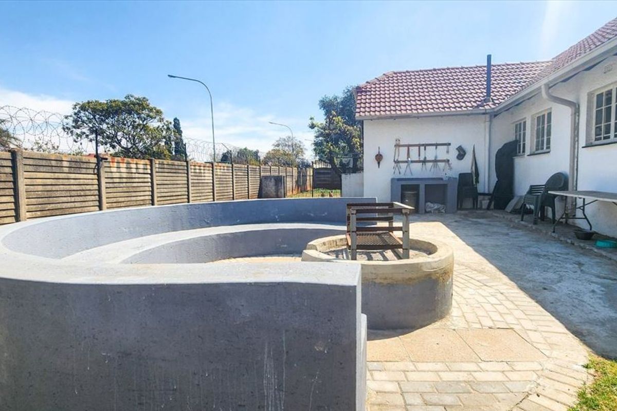 Rear exterior area featuring a paved patio, built-in fire pit with curved concrete seating, and a built-in braai area against the house wall.