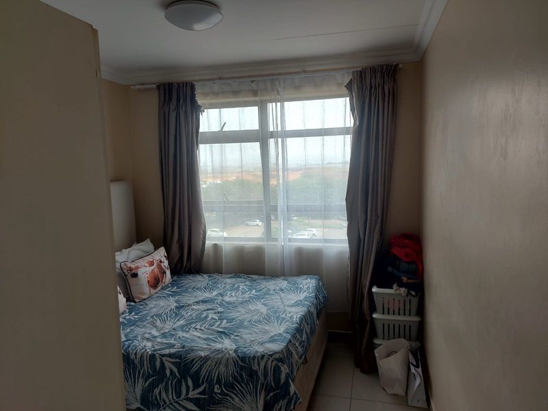A compact bedroom featuring tiled flooring and a large window that provides natural light and an exterior view.