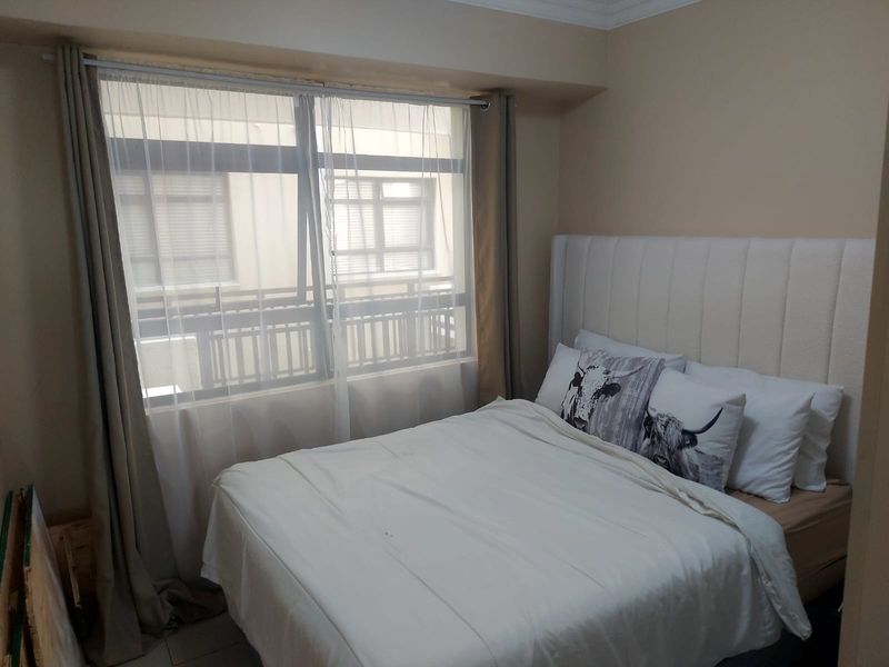 A cozy bedroom featuring a large window with natural light, a built-in headboard, and neutral wall tones.