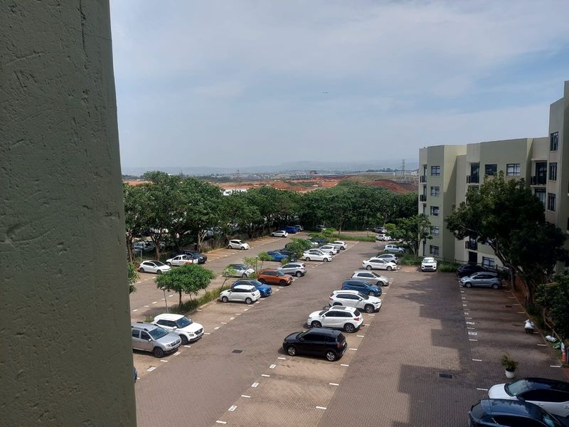 Elevated view overlooking the apartment complex parking area, surrounding trees, and distant landscape.