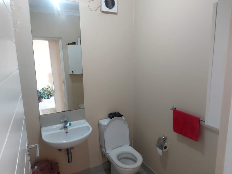 A functional bathroom featuring a wall-mounted basin, toilet, and extractor fan, with a large wall mirror and towel rail.