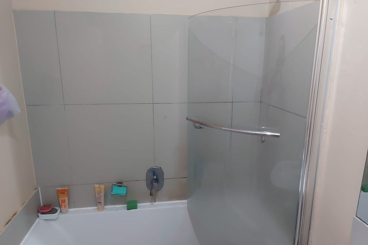 A functional bathroom featuring a bathtub with a glass shower screen, mixer tap, and tiled wall surround.