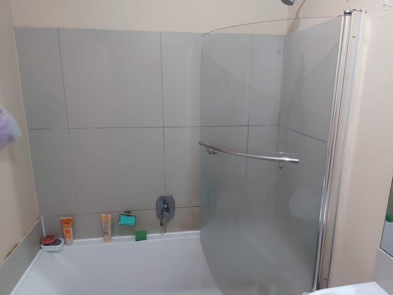 A functional bathroom featuring a bathtub with a glass shower screen, mixer tap, and tiled wall surround.