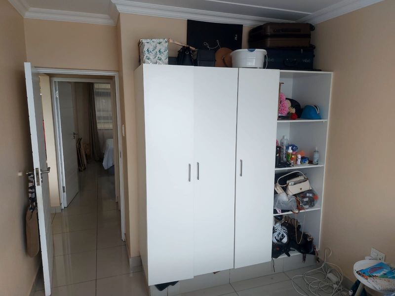 A bedroom featuring a white built-in wardrobe with open shelving and tiled flooring, leading to an adjacent room through an internal doorway.