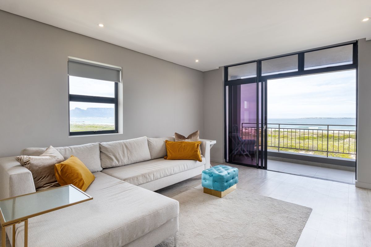 Bright and modern living room featuring large sliding glass doors leading to a balcony with scenic coastal views and recessed ceiling lighting.
