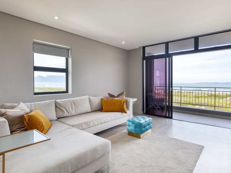 Bright and modern living room featuring large sliding glass doors leading to a balcony with scenic coastal views and recessed ceiling lighting.