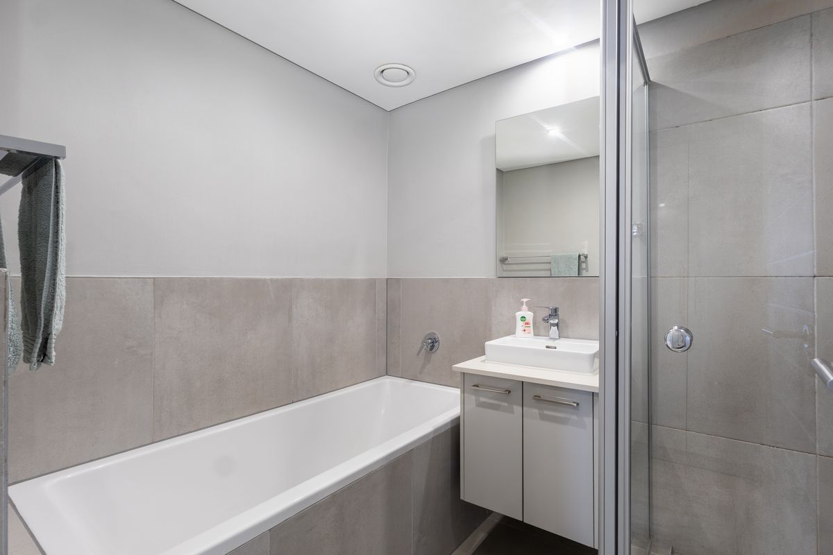Modern bathroom featuring a built-in bathtub, wall-mounted vanity with vessel sink, and a separate glass-enclosed shower with neutral grey tiling.