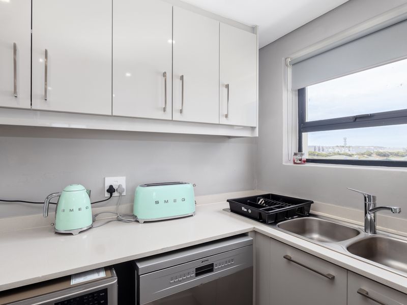 Modern kitchen featuring white gloss cabinetry, stone countertops, stainless steel double sink, and integrated dishwasher, offering a clean and functional workspace.
