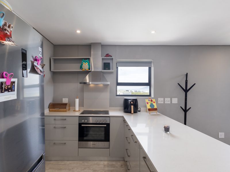 Modern kitchen featuring sleek grey cabinetry, quartz countertops, built-in oven, electric hob, and a stainless steel extractor fan with recessed lighting.
