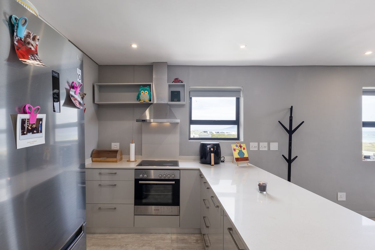 Modern kitchen featuring sleek grey cabinetry, quartz countertops, built-in oven, electric hob, and a stainless steel extractor fan with recessed lighting.