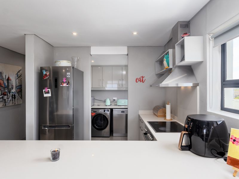 Modern kitchen featuring sleek cabinetry, stone countertops, integrated appliances, and a functional scullery area with laundry facilities.