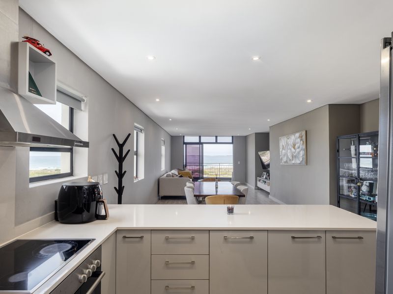Modern open-plan kitchen and living area featuring sleek cabinetry, quartz countertops, integrated appliances, and seamless flow to a balcony with coastal views.