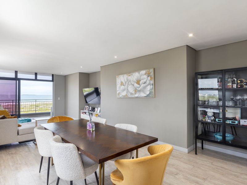 Spacious open-plan living and dining area featuring modern laminate flooring, recessed lighting, and large sliding doors leading to a balcony with ocean views.