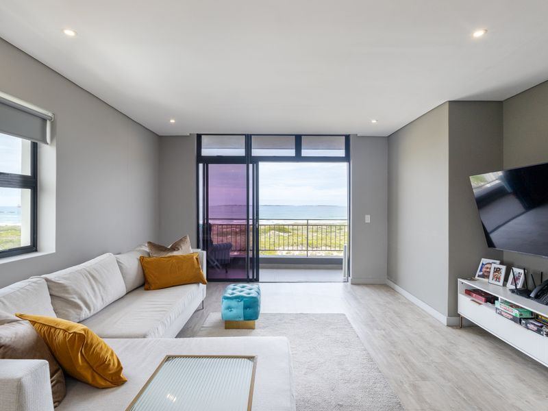 Modern living room featuring laminate flooring, recessed lighting, and large sliding glass doors opening onto a balcony with scenic coastal views.