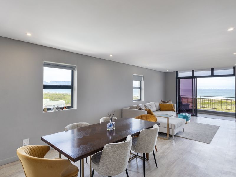 Spacious open-plan living and dining area featuring modern laminate flooring, recessed lighting, and large sliding doors opening to a balcony with ocean views.