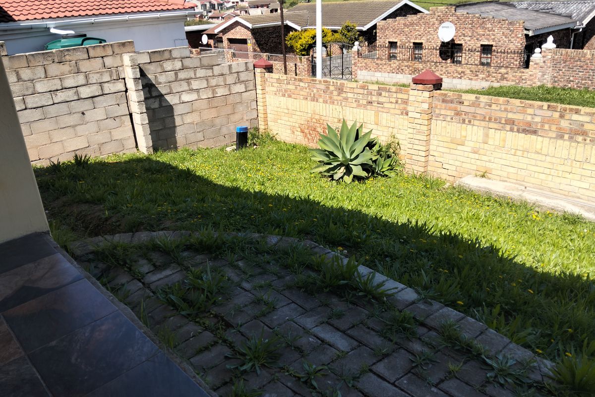 A rear garden area featuring a paved patio, lawn, and brick boundary walls, requiring landscaping and maintenance to improve its overall appeal.