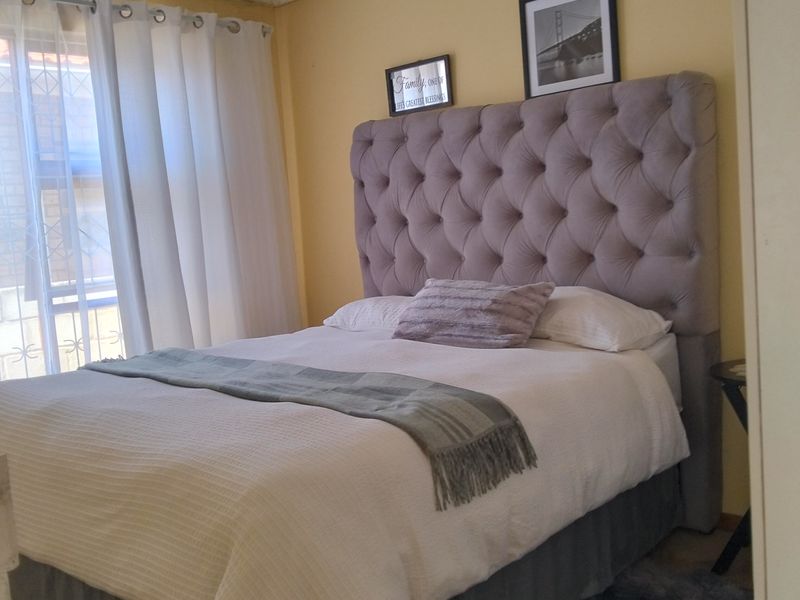 A cozy bedroom featuring a tufted headboard, built-in wardrobe, and natural light from the window. The space offers a comfortable and functional layout.