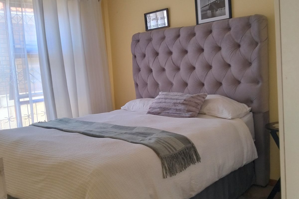 A cozy bedroom featuring a tufted headboard, built-in wardrobe, and natural light from the window. The space offers a comfortable and functional layout.