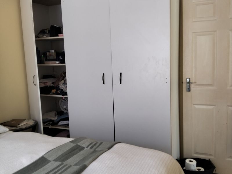 A bedroom featuring a white built-in wardrobe with shelving and a standard panel door, finished with simple cove cornicing.