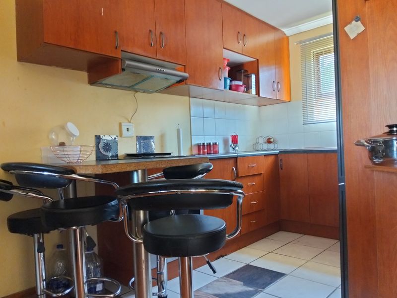 Compact kitchen featuring wood-tone cabinetry, laminate countertops, a breakfast bar, and tiled flooring, offering a functional layout with integrated extractor fan.