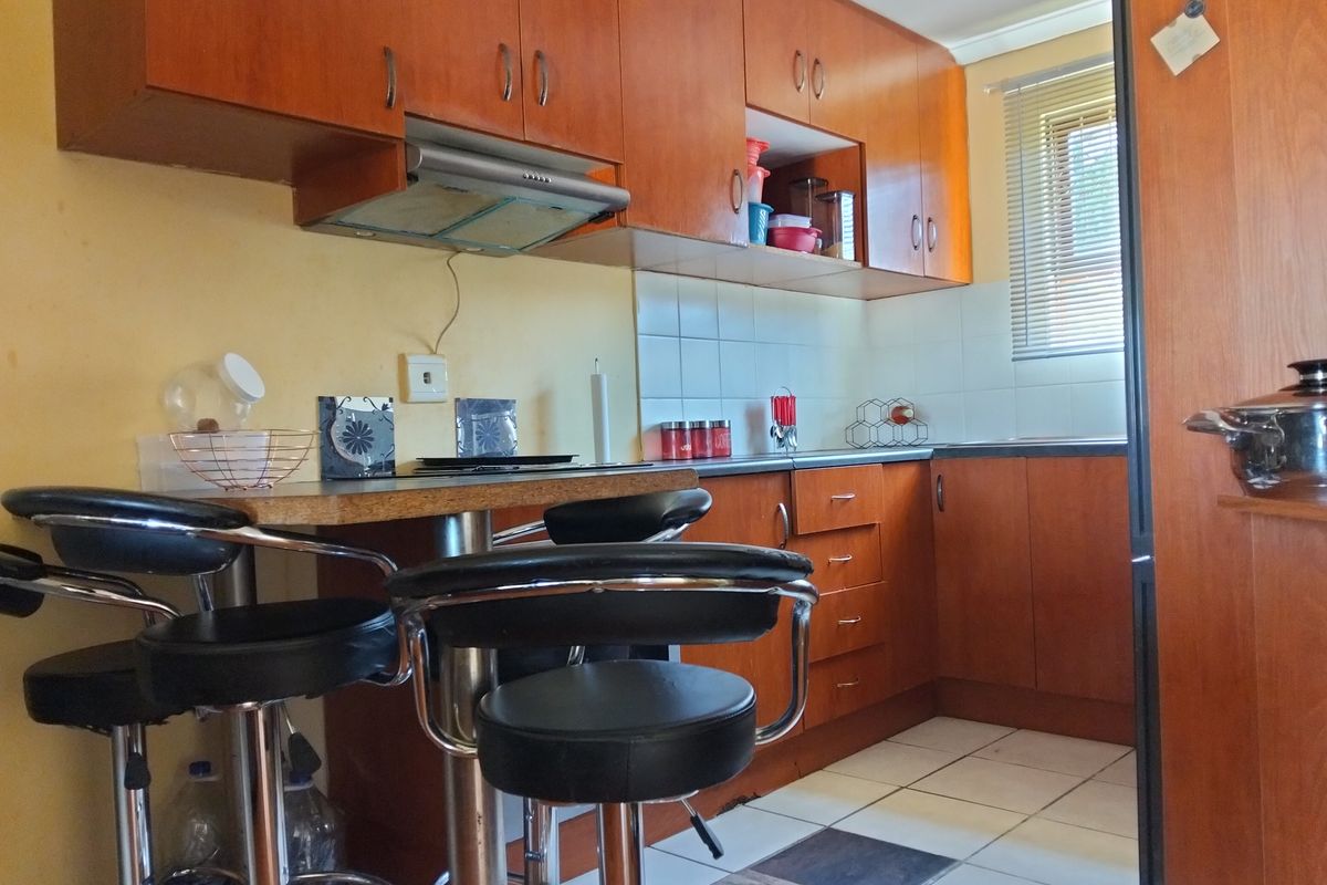Compact kitchen featuring wood-tone cabinetry, laminate countertops, a breakfast bar, and tiled flooring, offering a functional layout with integrated extractor fan.