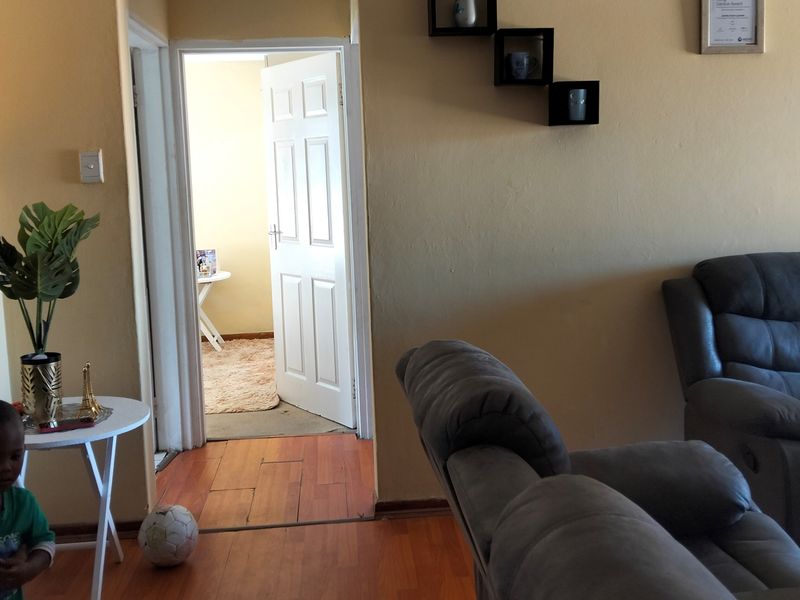 A living room area featuring laminate flooring and a doorway leading to an adjacent room, with visible wear on the ceiling and wall finishes.