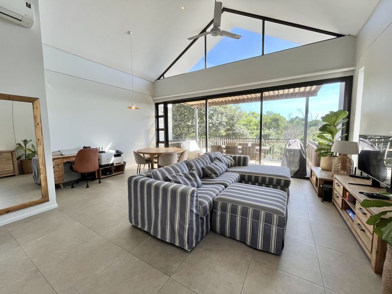 Spacious open-plan living area featuring high vaulted ceilings, large sliding glass doors leading to a balcony, and modern tiled flooring.