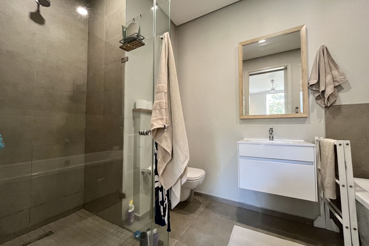Modern bathroom featuring a walk-in shower with glass screen, wall-mounted vanity, and contemporary wall-mounted toilet with neutral tiling.