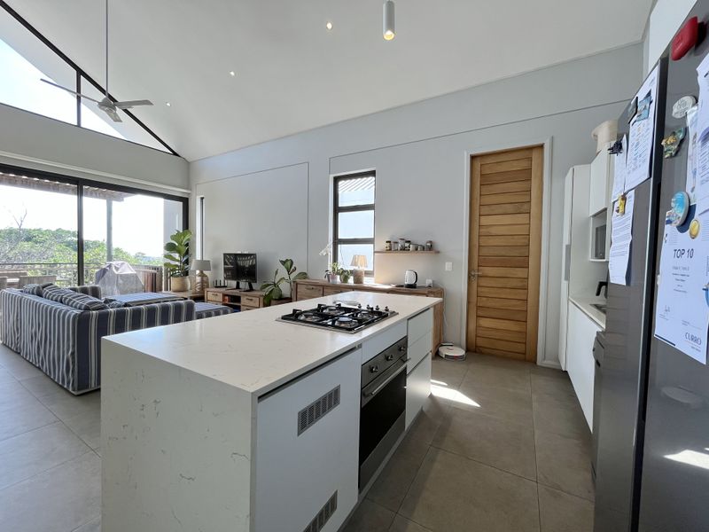 Spacious open-plan kitchen and living area featuring a central island with gas hob, modern finishes, high ceilings, and large sliding doors leading to the patio.