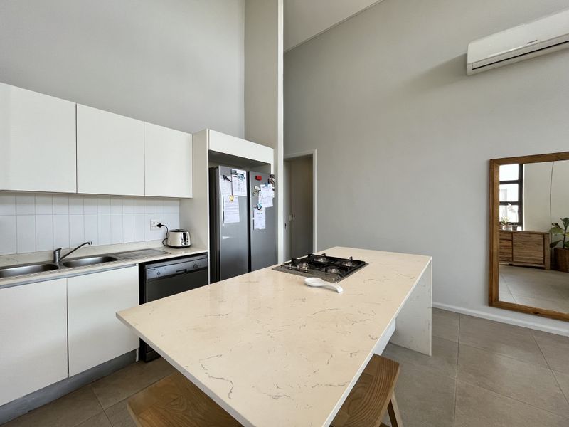 Modern kitchen featuring white cabinetry, stone countertops, a central island with a gas hob, and tiled flooring in an open-plan layout.