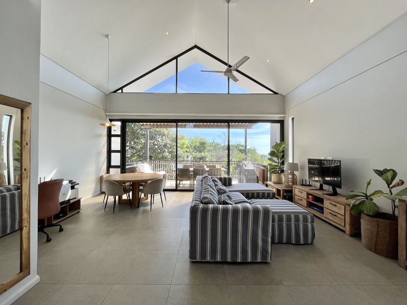 Spacious open-plan living and dining area featuring a dramatic vaulted ceiling, large sliding doors leading to a balcony, and modern tiled flooring.