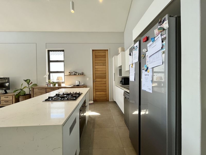 Modern kitchen featuring a central island with a gas hob, stone countertops, sleek cabinetry, and tiled flooring, leading to a wooden interior door.