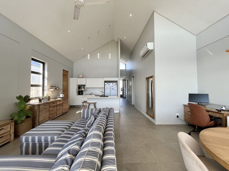 Spacious open-plan living area featuring a vaulted ceiling, tiled floors, modern kitchen with island, and split-system air conditioning in a well-maintained apartment setting.