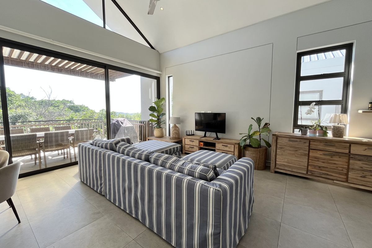 Spacious living room featuring high vaulted ceilings, large sliding glass doors leading to a balcony, and modern tiled flooring with abundant natural light.