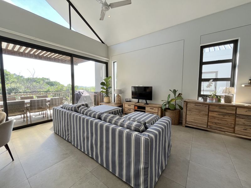 Spacious living room featuring high vaulted ceilings, large sliding glass doors leading to a balcony, and modern tiled flooring with abundant natural light.