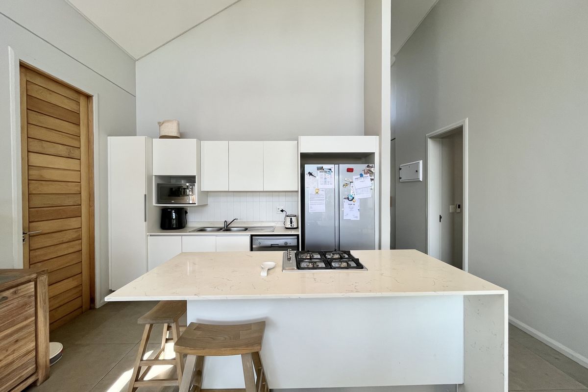 Modern kitchen featuring white cabinetry, stone countertops, a central island with a gas hob, and a high vaulted ceiling.