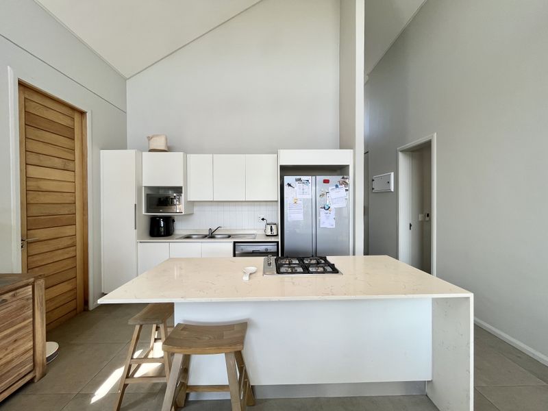 Modern kitchen featuring white cabinetry, stone countertops, a central island with a gas hob, and a high vaulted ceiling.