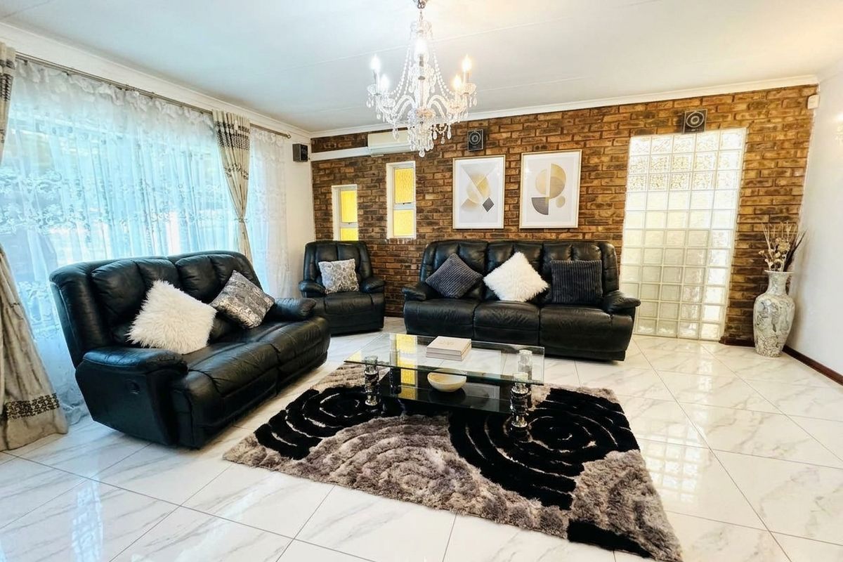Spacious living room featuring a striking exposed brick wall, elegant crystal chandelier, modern porcelain floor tiles, and a unique glass block feature window.