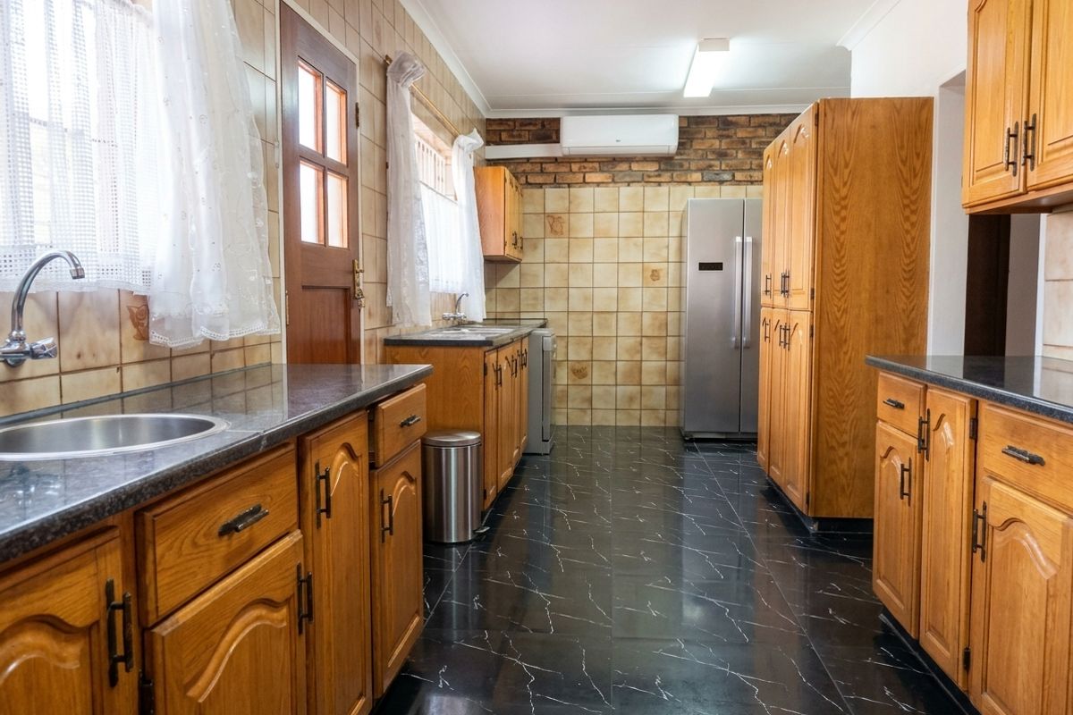 A functional kitchen featuring wooden cabinetry, dark laminate countertops, tiled backsplash, and black marble-effect floor tiles with an integrated air conditioning unit.