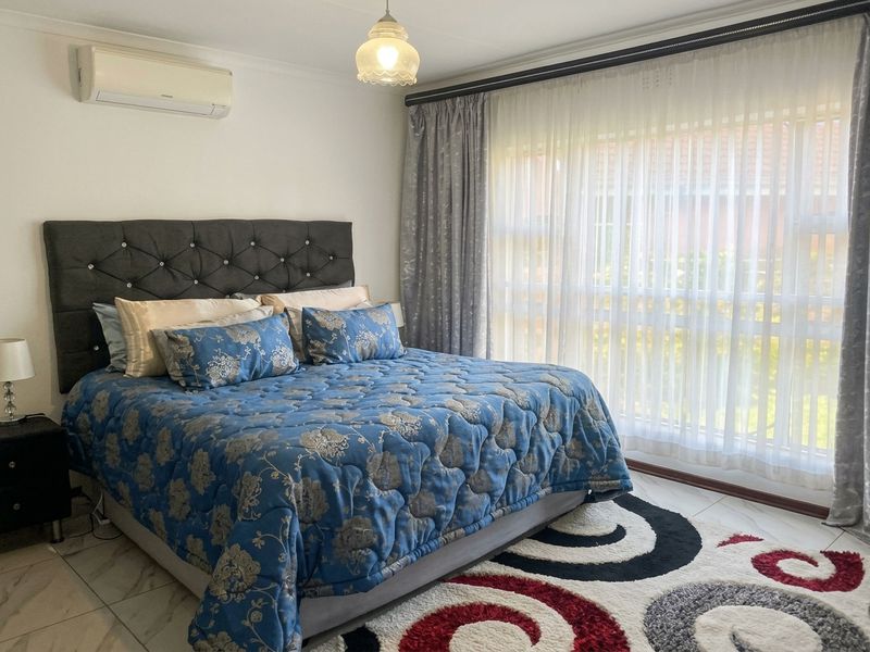 A well-maintained bedroom featuring tiled flooring, a large window with curtain tracks, and a wall-mounted air conditioning unit.