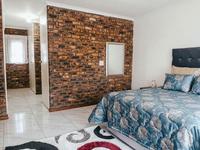 A well-maintained bedroom featuring a distinctive exposed brick feature wall, neutral tiled flooring, and integrated built-in storage solutions.
