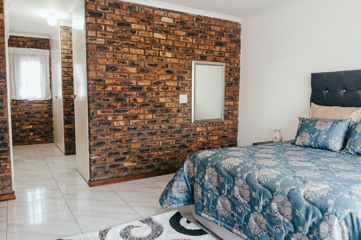 A well-maintained bedroom featuring a distinctive exposed brick feature wall, neutral tiled flooring, and integrated built-in storage solutions.